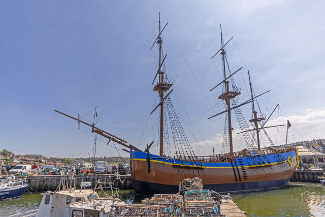 A replica of HMS Endeavour moored in Whitby Harbour. The colourful hull is in the foreground with masts projecting upwards.