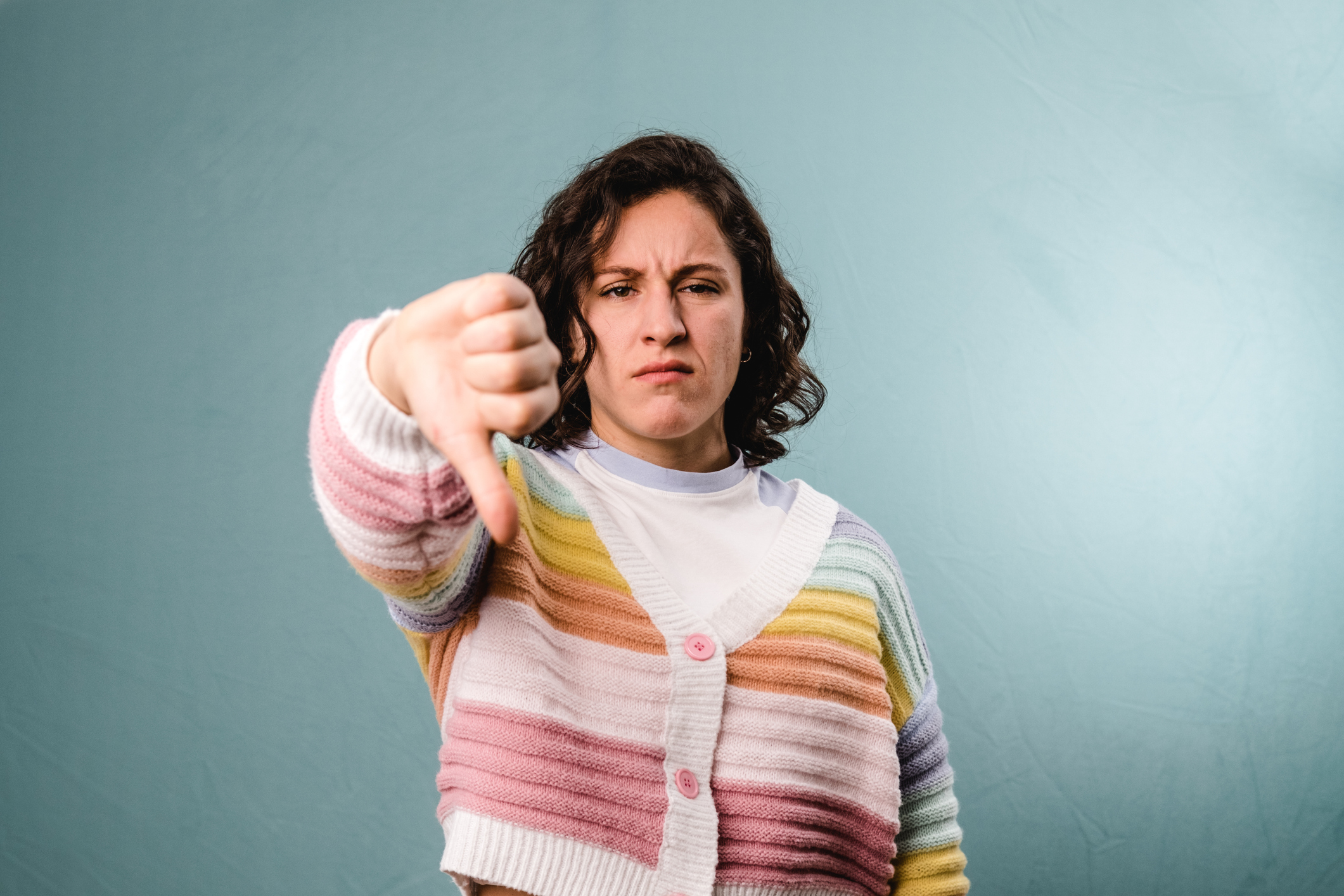 Unsatisfied spanish woman showing thumb down disapproval gesture with angry expression on blue background