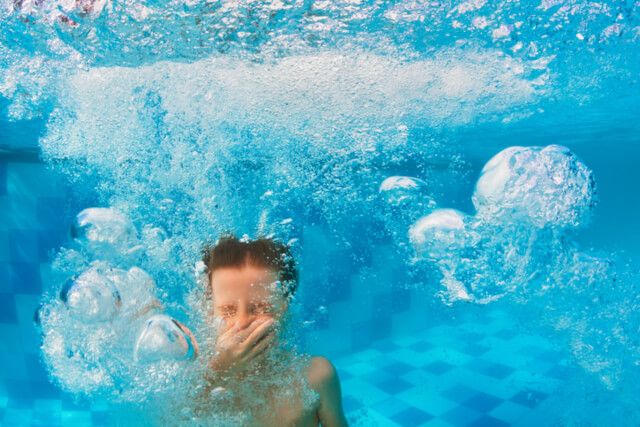 A boy holding his nose after diving into a swimming pool