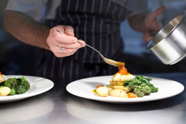 A chef serving a dish of seafood potatoes and veg