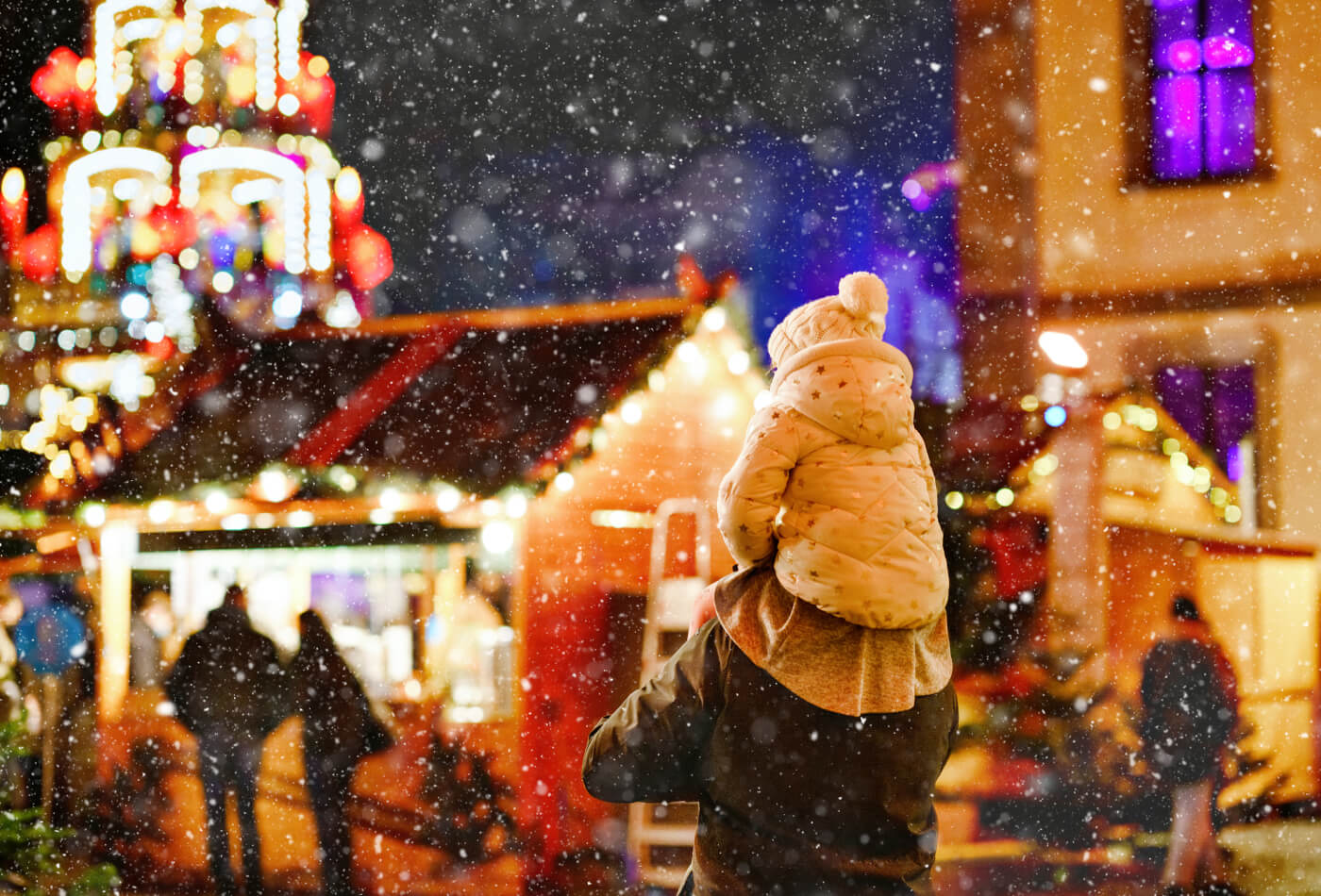 A child sat on an adult shoulders in the snow at a Christmas market