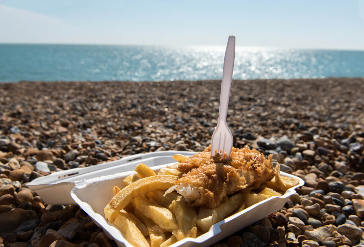 A takeaway portion of fish and chips sat on a rocky beach