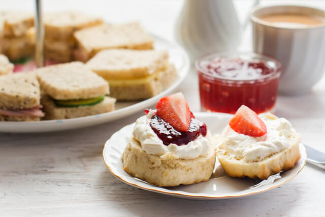 Scones with jam and cream and a plate of cut sandwiches