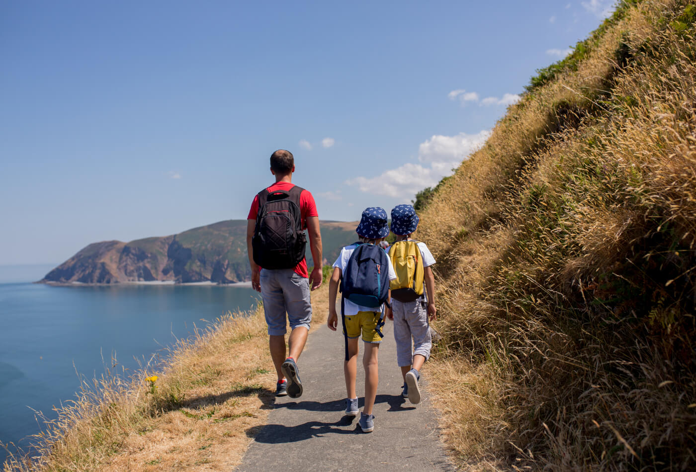 A father and two young children walking along a coastal path with cliffs in the far distance