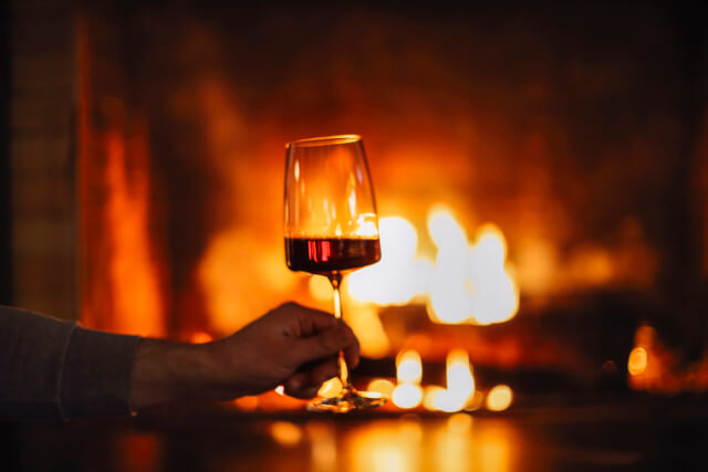 A glass of wine held infront of a roaring fire