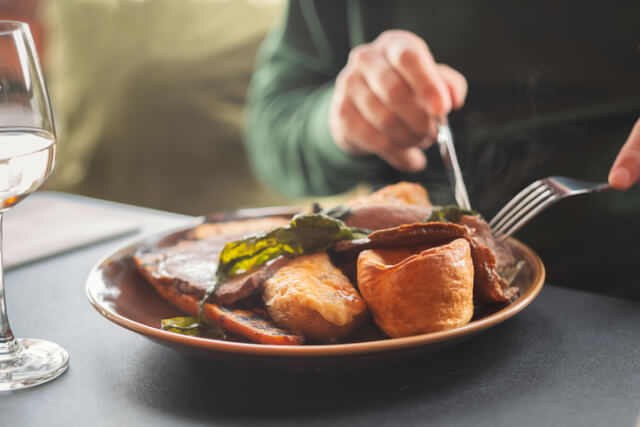 A person using a knife and fork to cut into a beef dinner on a plate