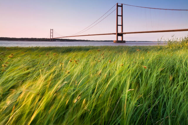 A view across a grassy field to Humber Bridge in the distance