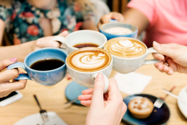 Five friends toasting mugs of coffee around a table in a cafe