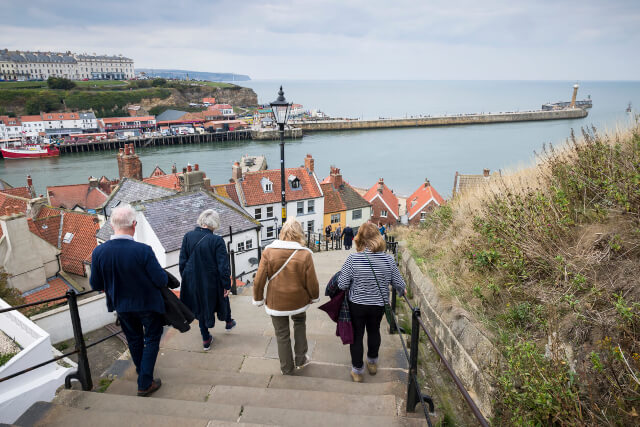 Four people walking down Whitby Steps with a view of the coast in the background