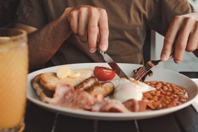 Someone cutting a fried egg on their english breakfast at a table