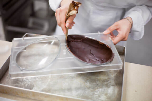 A chocolatier using an egg mould to create a chocolate easter egg 
