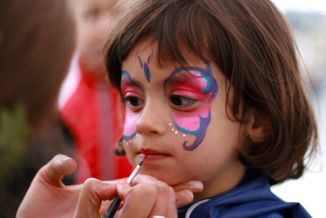 A little girl with a pink and blue butterfly being painted on her face