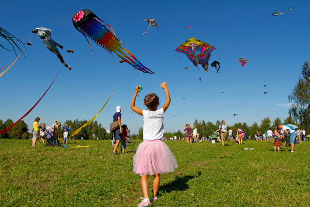 A young girl in a pink skirt waving at kites flying overhead 
