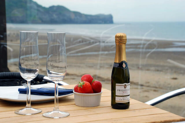 Prosecco and strawberries on a table at Sandside Cafe with a view of the sea in the background