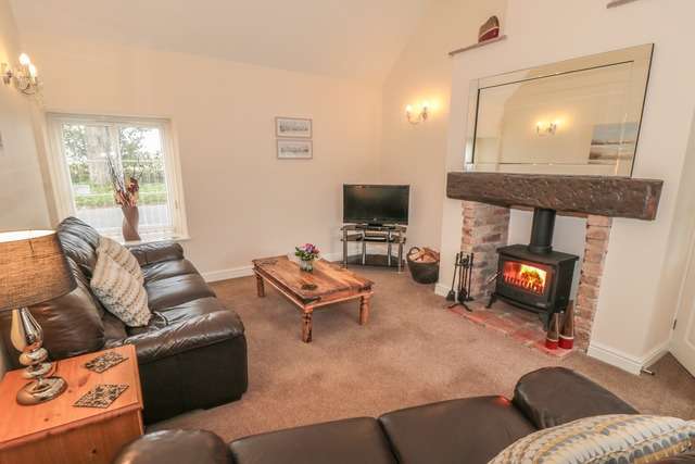 Bright living room with dark leather sofas, a rustic wooden coffee table, and a brick fireplace featuring a wood-burning stove beneath a large wall mirror.