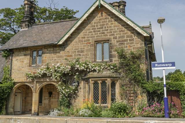 Charming stone-built house with arched doorways, leaded windows, and climbing plants, situated beside the Ruswarp railway station sign.
